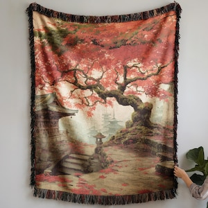 Könnte beinhalten: Ein gewebtes Wandtuch mit einer japanischen Gartenszene, einem großen Baum mit roten Blättern, Steinlaternen und Pagoden. Das Wandtuch hat einen Fransenrand und wird an einer Wand präsentiert.