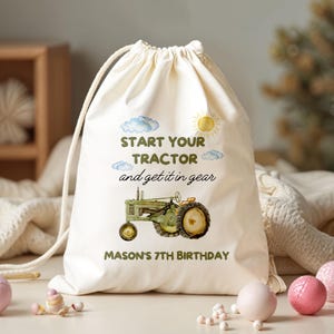 Könnte beinhalten: Ein cremefarbener Kordelzugbeutel mit einer Aquarellillustration eines grünen Traktors, einer Sonne und Wolken. Der Text lautet "Start Your Tractor and get it in gear" und "Mason's 7th Birthday".