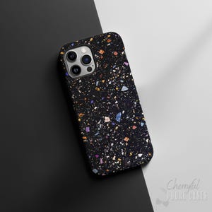 Könnte beinhalten: Schwarze Handyhülle mit Terrazzo-Muster. Die Hülle hat ein gesprenkeltes Design mit farbenfrohen Fragmenten in Blau-, Gelb-, Orange- und Lilatönen. Die Hülle hat ein glänzendes Finish und einen Kameraausschnitt.