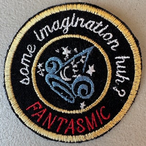 May include: Round black embroidered patch with gold and white trim. The patch features the words "some imagination huh?" and "FANTASMIC" in white and red lettering. A blue and white design is in the center.