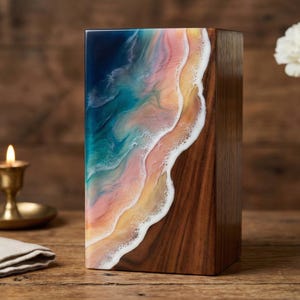 Peut inclure: Un coffret rectangulaire en bois avec une façade en résine représentant une scène de plage. L'art en résine présente des nuances de bleu, turquoise, rose, jaune et blanc, ressemblant à des vagues et du sable. Les côtés sont en bois foncé.