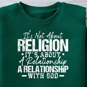 Puede incluir: Una sudadera verde oscuro con el texto blanco: "It's Not About RELIGION It's About A Relationship A RELATIONSHIP WITH GOD". El texto está centrado y tiene un aspecto desgastado y texturizado.