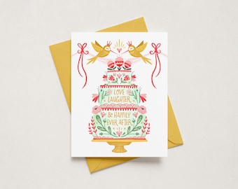 May include: A white greeting card featuring a three-tiered cake illustration with pink flowers, green foliage, and two gold birds wearing crowns. The text reads LOVE LAUGHTER & HAPPILY EVER AFTER. The card is placed on a mustard yellow envelope.