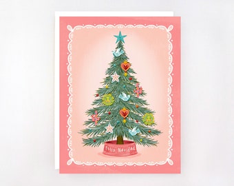 May include: A Christmas card featuring a decorated Christmas tree with ornaments, birds, and a star on top. The tree is set against a pink background with a scalloped border. The words "Feliz Navidad" are written on the tree base.