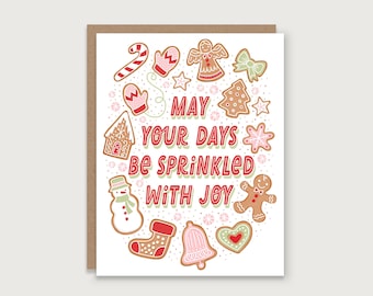 May include: A holiday greeting card with a brown border. The card features various gingerbread cookie designs, including a snowman, angel, and gingerbread man. The text "May Your Days Be Sprinkled With Joy" is written in red and green.