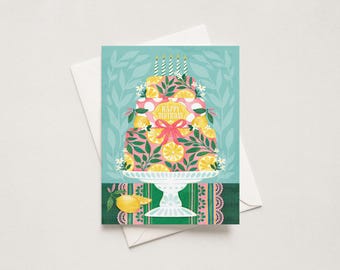 May include: A rectangular greeting card featuring a three-tiered cake on a white pedestal stand. The cake is decorated with pink and white polka dots, green leaves, yellow lemon slices, and a pink ribbon. The text HAPPY BIRTHDAY is centered.
