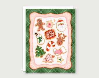 May include: A greeting card featuring a collection of illustrated Christmas cookies. The cookies include a gingerbread man, snowman, Santa, reindeer, Christmas tree, and candy cane. The card has a green plaid background and a pink scalloped border. Text reads "Sweet Holiday Wishes."
