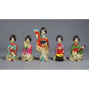 Op de afbeelding: Vijf kleine keramische beeldjes van Japanse vrouwen in traditionele kleding. Elk beeldje is geschilderd in felle kleuren en heeft een uniek ontwerp. De vrouwen houden verschillende instrumenten vast, waaronder een waaier, een trommel en een fluit.