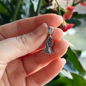 Puede incluir: Un charm de plata con el Trono de Hierro de la serie de televisión Juego de Tronos. El charm tiene la forma del trono con espadas y una corona en la parte superior. El charm tiene las palabras "Game of Thrones" inscritas en la parte posterior.