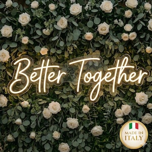 Puede incluir: Un letrero de neón que dice "Better Together" en una fuente cursiva, sobre un fondo de vegetación y rosas blancas. Un emblema dorado con la bandera italiana y el texto "Made in Italy" está en la esquina inferior derecha.