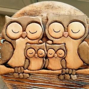 Peut inclure: Sculpture en bois représentant une famille de hiboux. L'œuvre présente deux grands hiboux et deux petits sur une branche. Les hiboux aux yeux fermés sont sculptés dans du bois brun clair et foncé, sur un fond en bois circulaire.