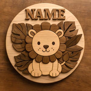 May include: Wooden round sign featuring a lion design with the word "NAME" at the top. The lion is light brown with a dark brown mane and is surrounded by dark brown leaves. The sign is made of light-colored wood.