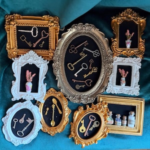 May include: A collection of ornate gold and white picture frames containing miniature objects including metal keys, small floral vases, gold spoons, and glass bottles with cork stoppers, all set against a dark background within each frame.