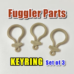 May include: Three tan keyrings with a loop design and a small rectangular base. The keyrings are arranged on a white background. The text "Fuggler Parts" is at the top, and "KEYRING Set of 3" is at the bottom.