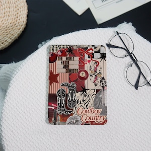 May include: A rectangular collage featuring cowboy-themed imagery. The design includes cowboy boots, stars, cherries, and the text "The World Needs More Cowboys" and "Cowboy Country". The color palette is dominated by red, black, and white.