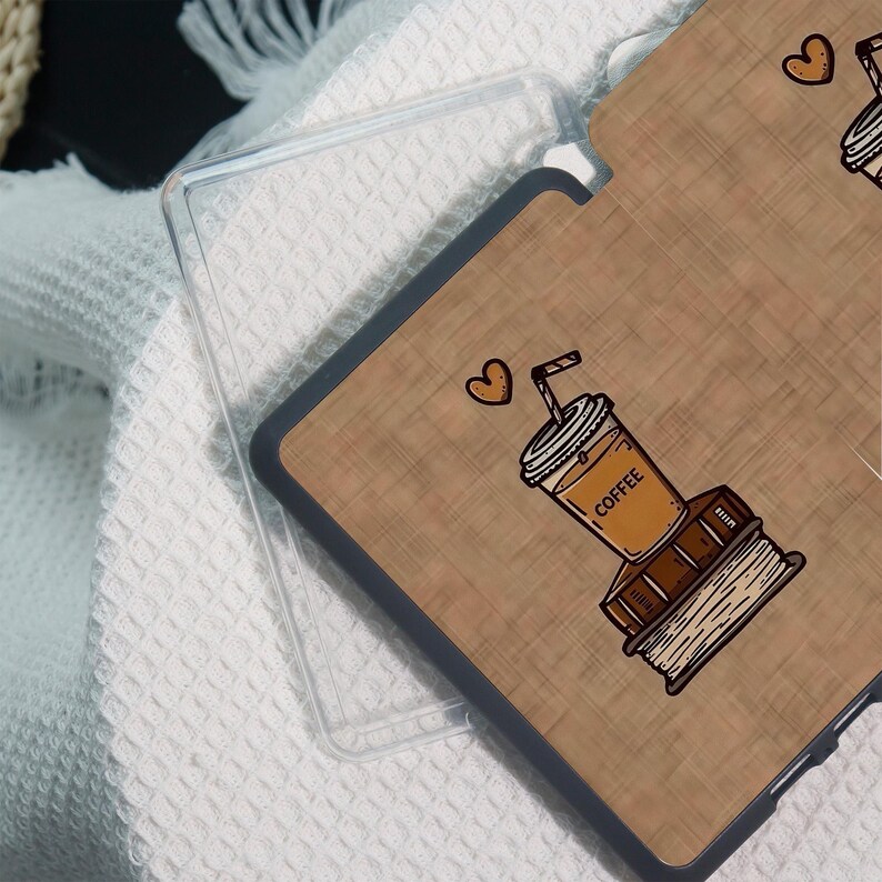 May include: A clear phone case with a brown, wood-grain design. The design features a coffee cup, a stack of books, and a heart. The word "COFFEE" is printed on the cup. The case is on a white, textured surface.