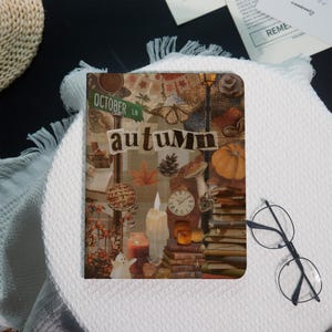 Könnte beinhalten: Ein dekoratives Notizbuch mit Herbstthema. Das Cover zeigt eine Collage mit dem Wort "Herbst" sowie Bildern von Kürbissen, Kerzen, Büchern und einem Straßenschild mit der Aufschrift "October Ln."