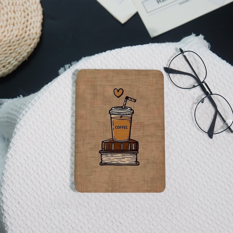 May include: A rectangular coaster with a brown background features a coffee cup illustration atop two books. The coffee cup has the word "COFFEE" printed on it, and a heart floats above it. A straw is in the cup. The coaster is on a white surface.