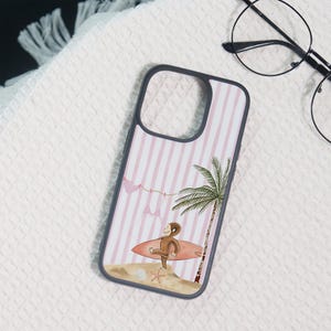 May include: A smartphone case featuring a light pink and white vertical striped background. The design includes a brown monkey sitting on a surfboard, a green palm tree, a starfish on the sand, and a clothesline with two pink bikini tops hanging.