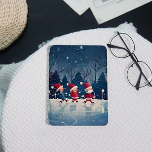 May include: A rectangular coaster featuring a winter scene with three figures in Santa hats ice skating. The background shows a snowy forest under a starry night sky. The figures are wearing red and blue outfits.