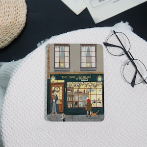 May include: A rectangular print featuring a detailed illustration of "The Book Exchange" storefront. The scene includes figures, a dog, and a cat. The building has two windows and a sign that reads "The Book Exchange".