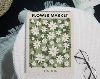 May include: A rectangular notebook with a light green cover featuring a repeating pattern of white daisies with yellow centers. The text FLOWER MARKET is printed in black at the top, and the word LONDON is printed in black at the bottom of the cover.