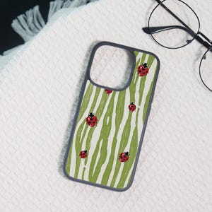 May include: A rectangular smartphone case with a dark gray border featuring a pattern of vertical olive green brushstrokes on a cream background, interspersed with small red ladybugs that have black spots and heart-shaped markings.