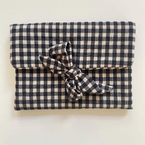 Puede incluir: Un bolso de mano con estampado de cuadros vichy en blanco y negro con cierre de lazo a juego. La tela es un material suave y tejido. El bolso de mano est&aacute; doblado y asegurado con un lazo grande.