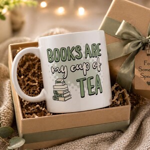May include: White ceramic mug with the text "BOOKS ARE my cup of TEA" in green and black lettering, with a stack of books illustration. The mug is in a gift box with a green ribbon and a tag that says "For Someone Special".