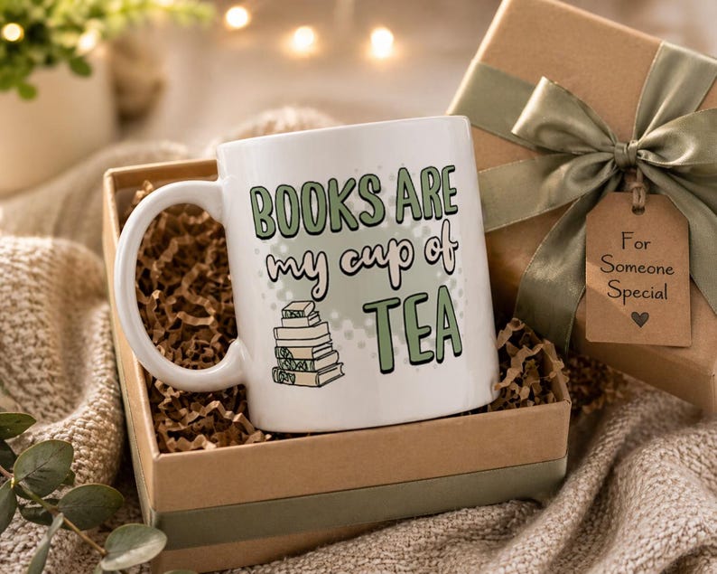 May include: White ceramic mug with the text "BOOKS ARE my cup of TEA" in green and black lettering, with a stack of books illustration. The mug is in a gift box with a green ribbon and a tag that says "For Someone Special".