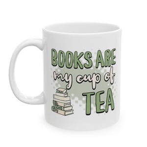 May include: White ceramic mug with the text "BOOKS ARE my cup of TEA" in green and black lettering. A stack of books is illustrated below the text. The mug has a curved handle.