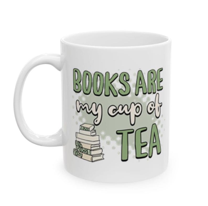 May include: White ceramic mug with the text "BOOKS ARE my cup of TEA" in green and black lettering. A stack of books is illustrated below the text. The mug has a curved handle.