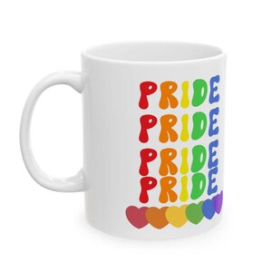 Puede incluir: Taza de cer&aacute;mica blanca con la palabra "PRIDE" en un arco&iacute;ris de colores repetida cinco veces. La palabra est&aacute; en una fuente en negrita y redondeada. En la parte inferior hay seis corazones coloridos. La taza tiene un asa blanca.
