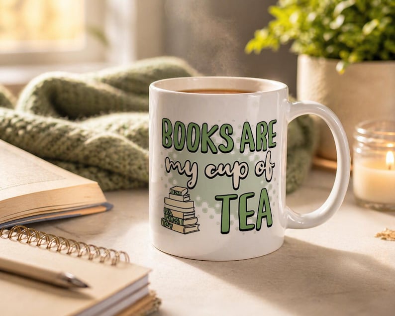 May include: White ceramic mug with the text "BOOKS ARE my cup of TEA" in green lettering. A stack of books is illustrated below the text. The mug is filled with a hot beverage, and steam rises from the top. A cozy reading theme.