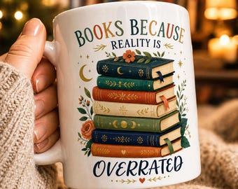 Op de afbeelding: Witte keramische mok met de tekst "BOOKS BECAUSE REALITY IS OVERRATED" en een stapel kleurrijke boeken. De boeken hebben bloemen- en hemelse ontwerpen. De mok wordt vastgehouden door een persoon die een beige trui draagt.