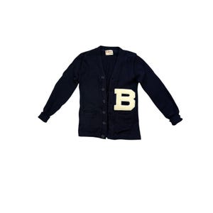 Könnte beinhalten: Marineblauer Cardigan mit großem weißem Filz-„B“-Aufnäher. Der Cardigan mit Knopfleiste hat lange Ärmel und zwei Vordertaschen. Das Etikett ist oben sichtbar. Ein klassischer Stil, geeignet für verschiedene Anlässe.