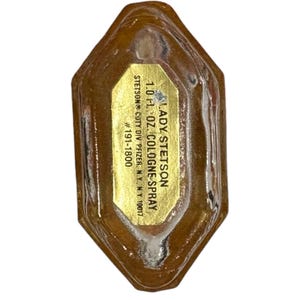 Peut inclure: Une bouteille de parfum Lady Stetson vintage. La bouteille est de couleur ambre clair avec une &eacute;tiquette dor&eacute;e. L'&eacute;tiquette indique "LADY STETSON 1.0 fl. oz. COLOGNE SPRAY". La bouteille porte le num&eacute;ro #191-1800.
