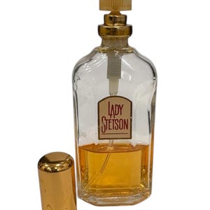 Peut inclure: Un flacon de parfum en verre transparent avec un bouchon dor&eacute; et un couvercle dor&eacute; s&eacute;par&eacute;. Le flacon porte une &eacute;tiquette avec l'inscription "LADY STETSON" dans un cadre rectangulaire. Le parfum &agrave; l'int&eacute;rieur est de couleur ambre.