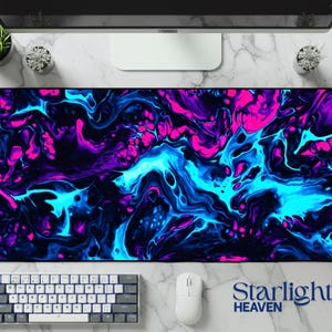 May include: A large rectangular mouse pad with a vibrant abstract design in shades of pink, blue, and purple. The design resembles flowing paint or liquid. A white keyboard and mouse are visible below the pad. The text "Starlight Heaven" is printed on the pad.