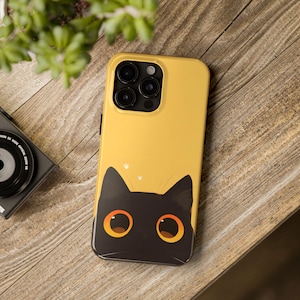 May include: A yellow phone case with a black cat peeking out from the bottom. The cat has large orange eyes.
