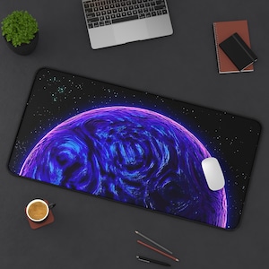 May include: A large rectangular mouse pad featuring a vibrant, swirling blue and purple planet design against a starry black background. A white computer mouse rests on the pad. Other items include a laptop, a small plant, and a cup of coffee.