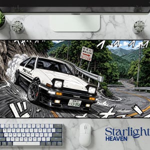 May include: A rectangular desk mat featuring a graphic illustration of a white and black Toyota AE86 Trueno drifting on a winding mountain road. The car displays the text Trueno on the front bumper and a Japanese license plate reading 13-954.