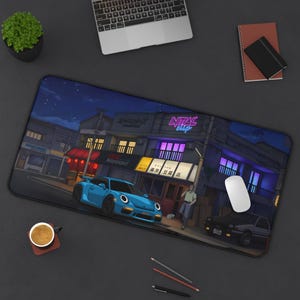 May include: A rectangular mouse mat depicting a nighttime anime scene with a blue sports car and a black car parked on a street. The scene includes buildings with neon signs and streetlights. A white mouse and a laptop are also visible.