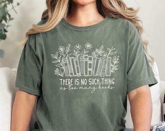 May include: Olive green t-shirt with a white graphic of books and floral elements. The text "THERE IS NO SUCH THING as too many books" is printed below the graphic. The shirt has short sleeves and a relaxed fit.
