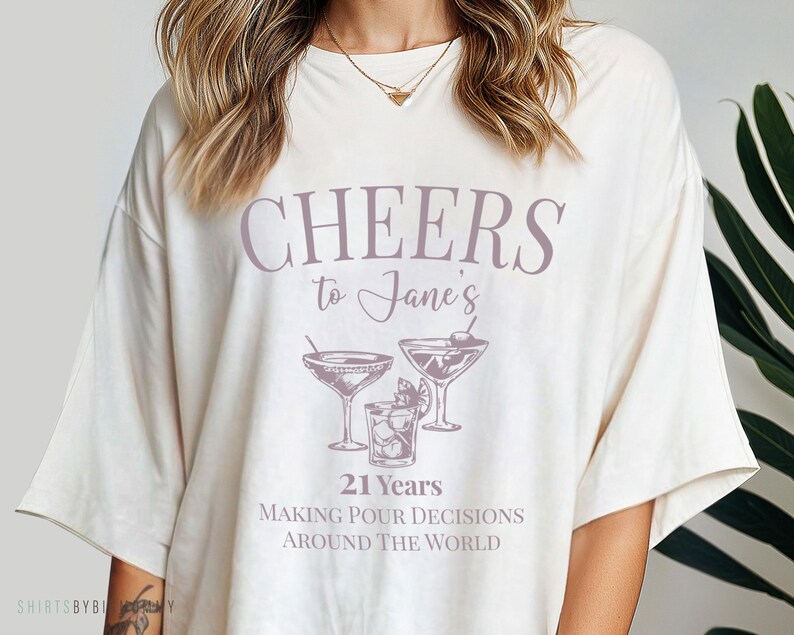 Peut inclure: T-shirt blanc avec le texte "Cheers to Jane's 21 Years Making Pour Decisions Around The World" et un graphique de trois verres &agrave; martini.