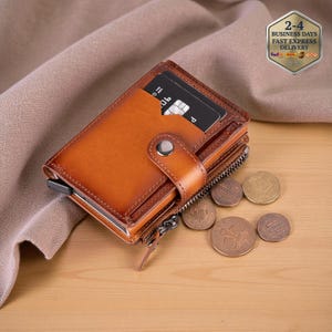 May include: A brown leather wallet with a snap closure and a zipper. A credit card is visible in a card slot. Several coins are scattered near the wallet. The wallet is on a wooden surface.