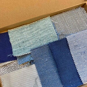 May include: A box containing fabric samples in a range of blue and grey hues. The samples are arranged in a grid pattern and feature different textures.