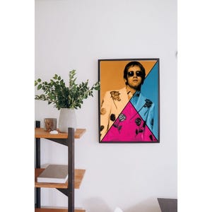 Può includere: Un poster incorniciato con un uomo che indossa un abito colorato con un motivo geometrico rosa, giallo e blu. L'uomo indossa occhiali da sole e ha un'espressione seria.