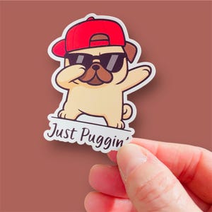 May include: A die-cut sticker featuring a tan pug wearing a bright red baseball cap and black sunglasses. The pug is performing a dab pose. Below the pug, the text Just Puggin' is printed in a dark brown script font on a white background.