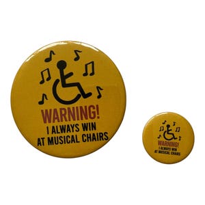 Può includere: Due spille circolari gialle con una grafica nera di una persona su una sedia a rotelle circondata da note musicali. Il testo recita WARNING! I ALWAYS WIN AT MUSICAL CHAIRS in caratteri neri e rossi. Le spille sono di dimensioni diverse.